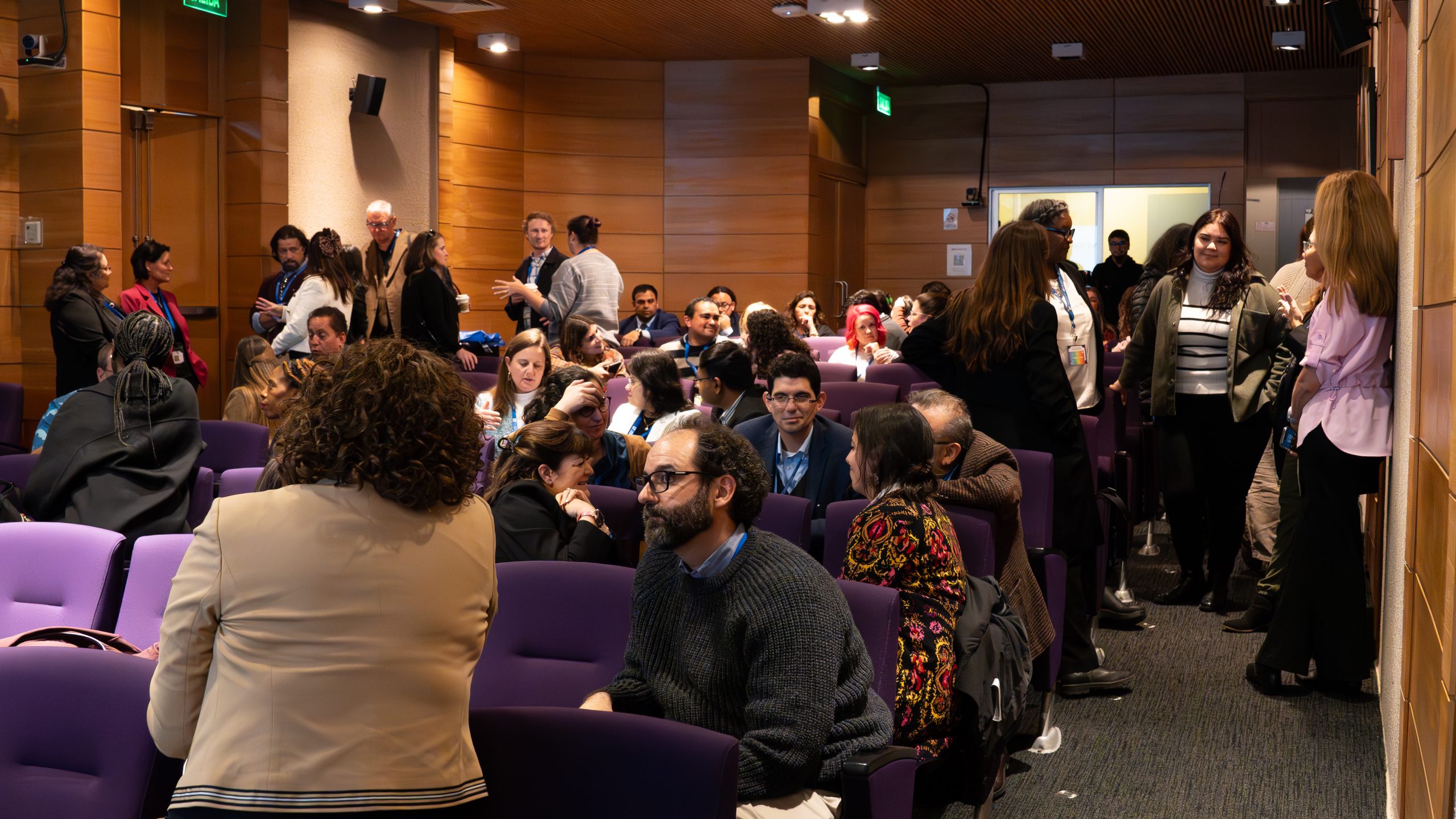 A lecture haul of people standing and speaking with their neighbors to discuss the content being shared at the symposium.